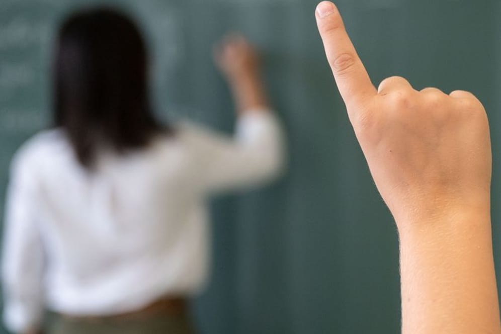 Ein Schüler meldet sich, während die Lehrerin an die Tafel schreibt (Symbolfoto): Besonders Frauen reduzieren häufig ihre Arbeitszeit.