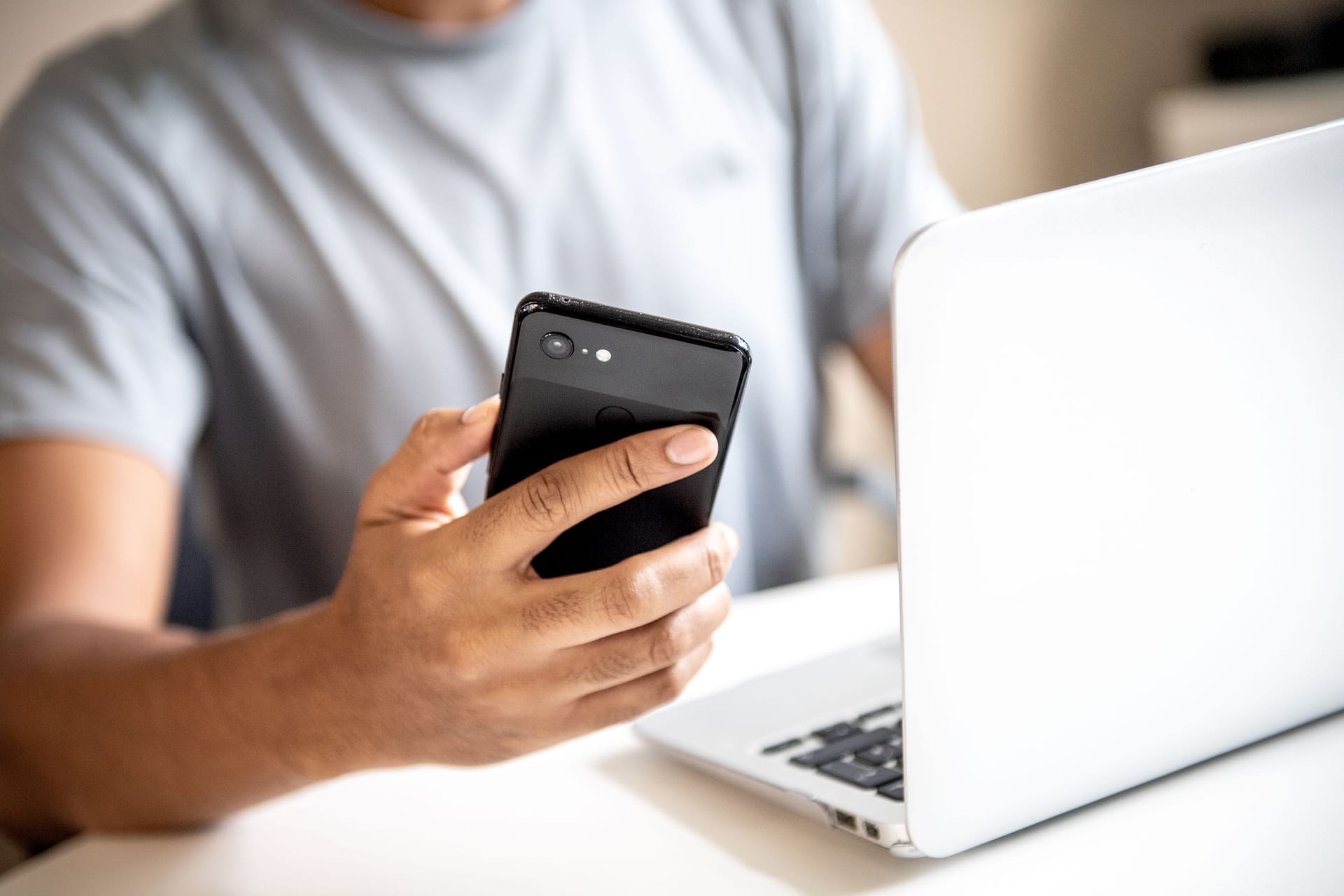 Ein junger Mann sitzt mit Smartphone vorm Laptop (Symbolbild): Steuern auf dem Smartphone erklären – mit "MeinELSTER+" soll es ganz einfach möglich sein.