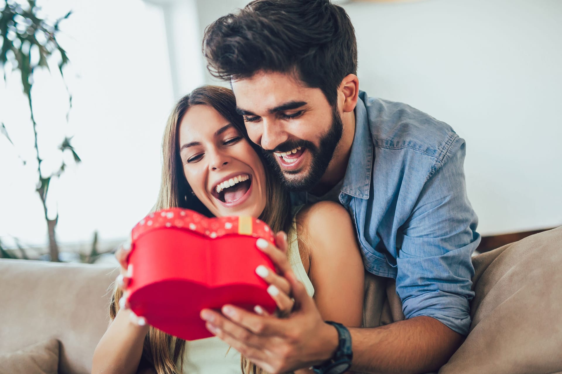 Beautiful young couple is celebrating at home. Handsome man is giving his girlfriend a gift box