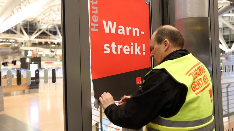 Ein Gewerkschaftsvertreter klebt ein Plakat mit der Aufschrift "Warnstreik!" an die Anzeigetafel vor das leere Terminal 2: Am Flughafen Hamburg sollen die Einschränkungen überschaubar bleiben.