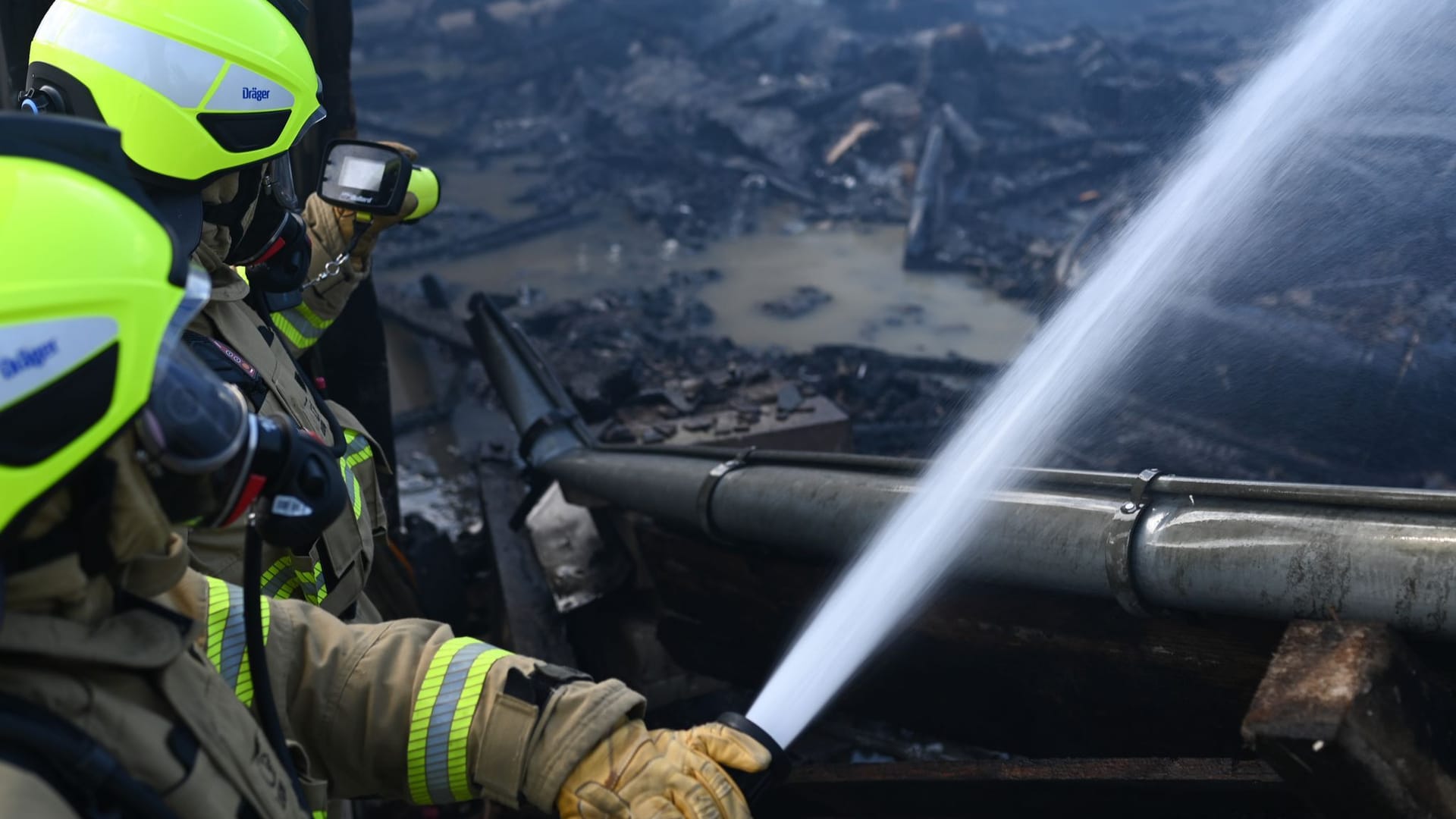 Feuerwehrmänner löschen das Feuer in der Halle und gucken mit einer Wärmebildkamera nach Glutnestern. Feuerwehrmänner löschen das Feuer in der Halle und gucken mit einer Wärmebildkamera nach Glutnestern.