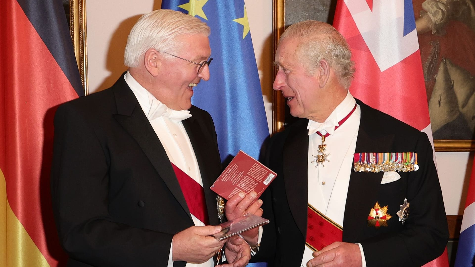 Bundespräsident Steinmeier und König Charles III. beim Defilee während des Staatsbanketts im Schloss Bellevue. Sie halten je eine CD in der Hand und lachen sich gegenseitig zu.