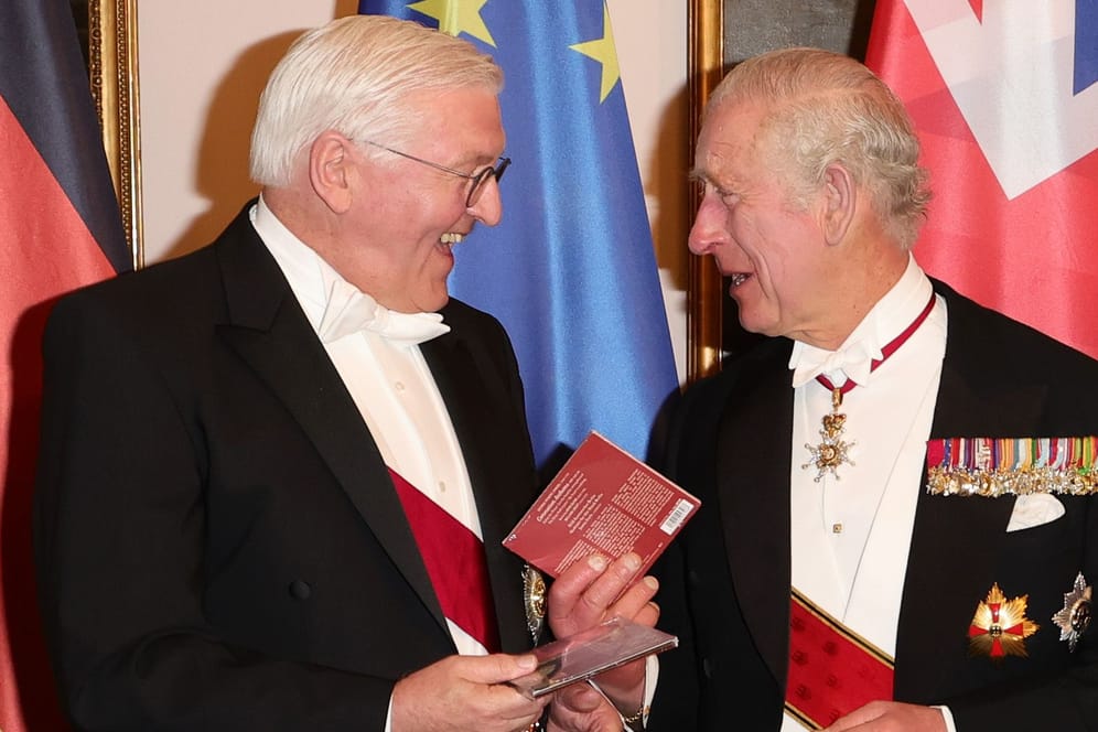 Bundespräsident Steinmeier und König Charles III. beim Defilee während des Staatsbanketts im Schloss Bellevue. Sie halten je eine CD in der Hand und lachen sich gegenseitig zu.