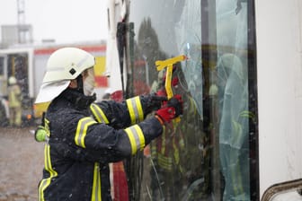 Ein Feuerwehrmann öffnet gewaltsam eine Busscheibe (Symbolfoto): Der Schulbus wurde von Ästen und Gebüschen gestützt.