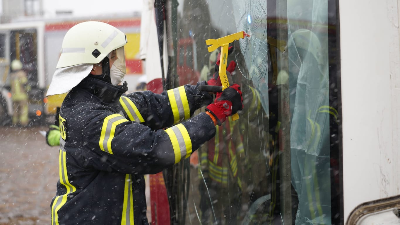 Ein Feuerwehrmann öffnet gewaltsam eine Busscheibe (Symbolfoto): Der Schulbus wurde von Ästen und Gebüschen gestützt.