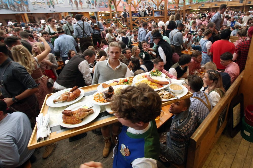 Ein Kellner balanciert ein volles Tablett mit Speisen durch ein Oktoberfestzelt (Archivbild): Geht es nach einer Münchner Initiative, soll es bis 2035 nur noch Bio auf dem Volksfest geben.