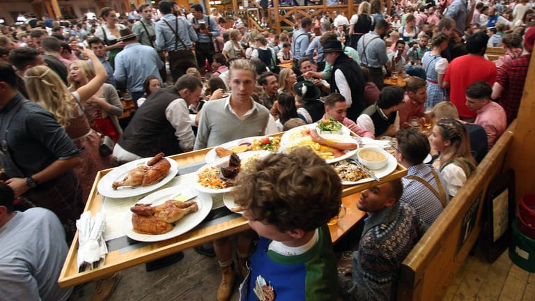 Ein Kellner balanciert ein volles Tablett mit Speisen durch ein Oktoberfestzelt (Archivbild): Geht es nach einer Münchner Initiative, soll es bis 2035 nur noch Bio auf dem Volksfest geben.