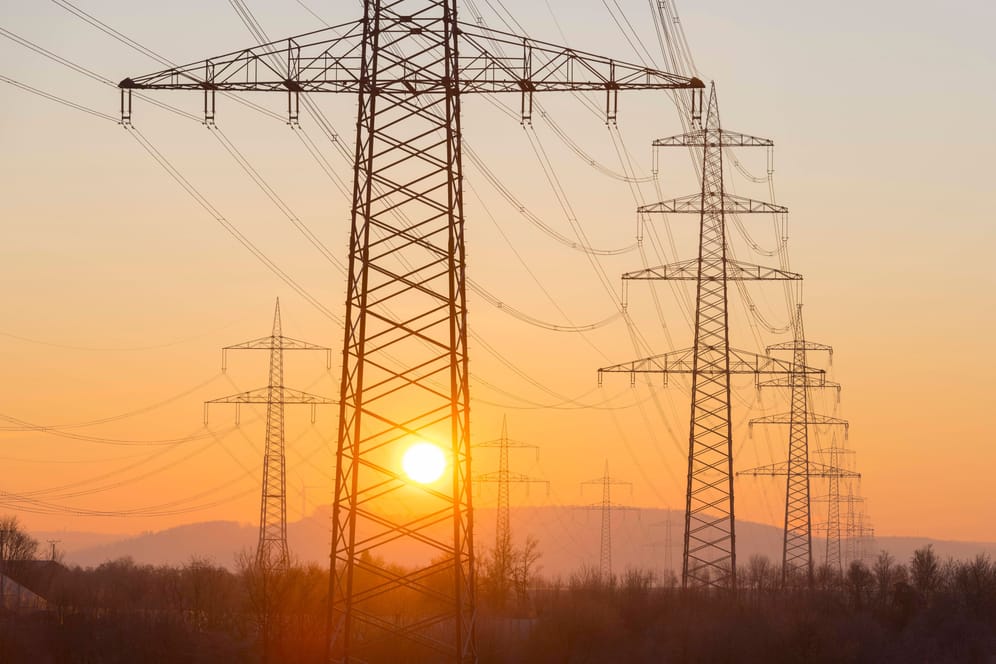 Strommasten bei Sonnenaufgang (Symbolbild): Noch immer kosten die Kilowattstunde Strom und Gas bei den meisten Grundversorgern mehr als der Preisdeckel vorsieht.