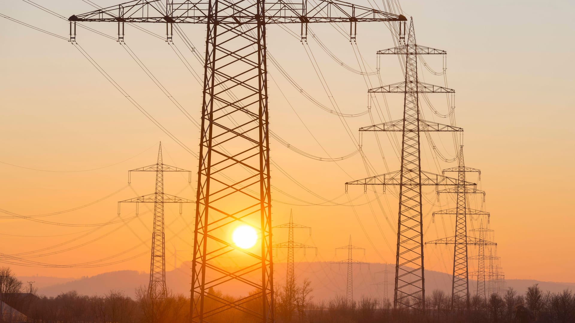 Strommasten bei Sonnenaufgang (Symbolbild): Noch immer kosten die Kilowattstunde Strom und Gas bei den meisten Grundversorgern mehr als der Preisdeckel vorsieht.