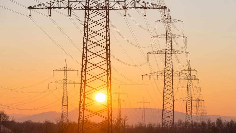 Strommasten bei Sonnenaufgang (Symbolbild): Noch immer kosten die Kilowattstunde Strom und Gas bei den meisten Grundversorgern mehr als der Preisdeckel vorsieht.
