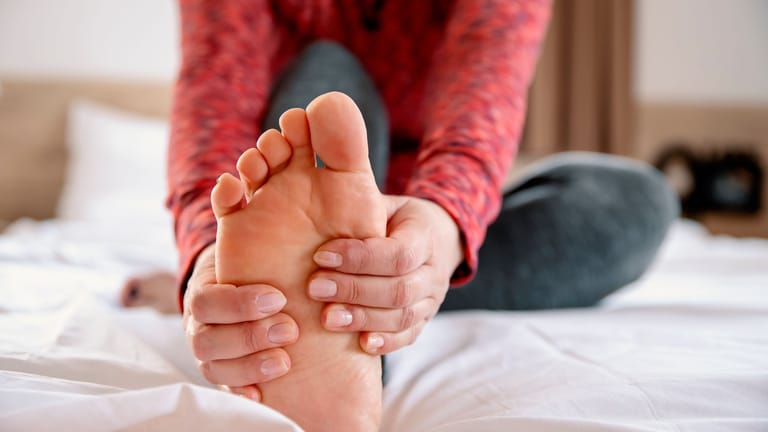 Eine Frau greift den rechten Fuß mit beiden Händen: Wer eine Plantarfasziitis hat, sollte regelmäßig bestimmte Übungen machen.