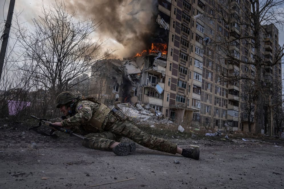Ein ukrainischer Polizist geht vor einem brennenden Gebäude in Deckung, das bei einem Luftangriff getroffen wurde.