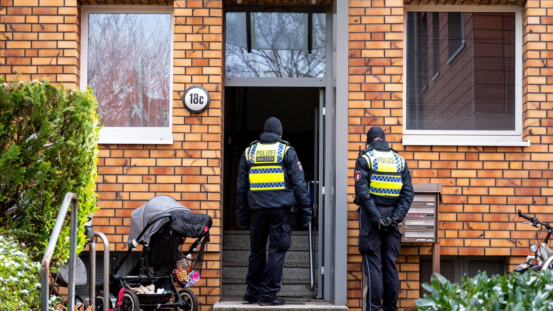 Polizisten stehen im Hamburger Stadtteil Stellingen vor einem Mehrfamilienhaus. Eine Hundertjährige soll dort von ihrem Enkel getötet worden sein.