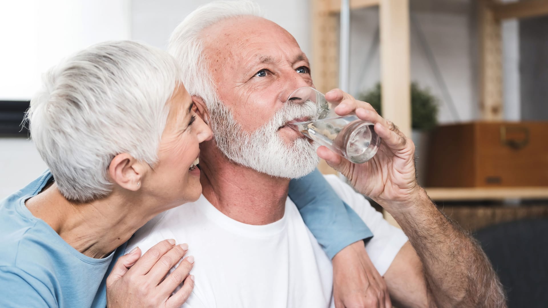 Ein Mann trinkt ein Glas Wasser und wird von einer Frau umarmt.