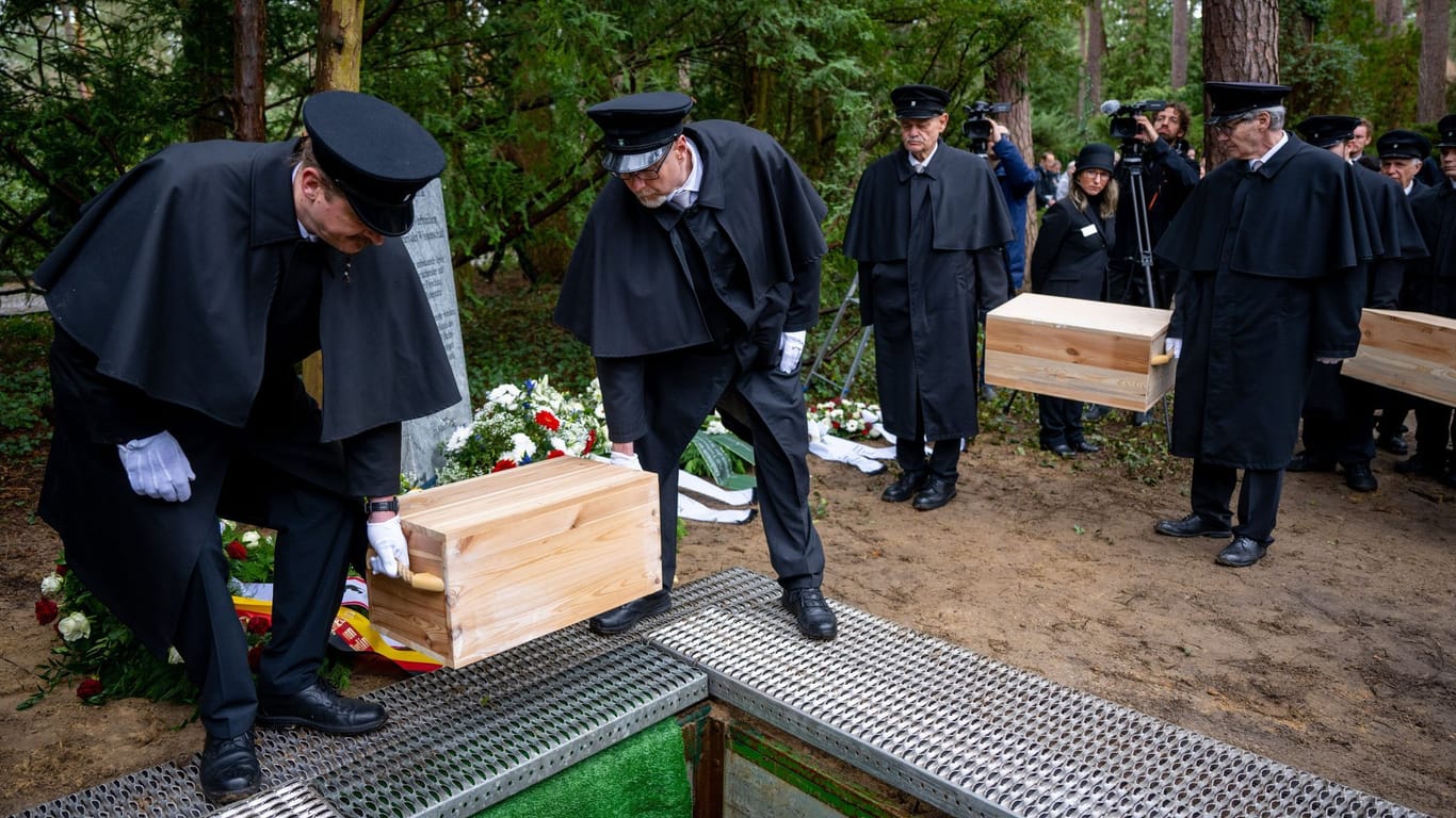 Gebeinekisten mit menschlichen Knochen werden in ein Grab auf dem Waldfriedhof Dahlem hinabgelassen. Die seit 2015 geborgenen menschlichen Überreste stammen teils von Opfern aus der NS-Zeit.