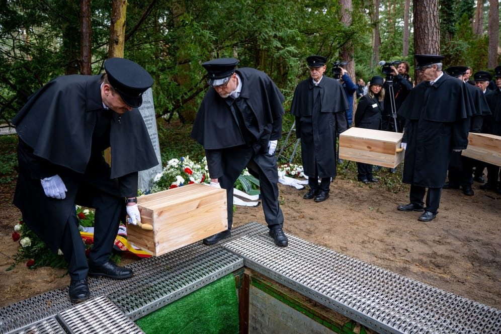 Gebeinekisten mit menschlichen Knochen werden in ein Grab auf dem Waldfriedhof Dahlem hinabgelassen. Die seit 2015 geborgenen menschlichen Überreste stammen teils von Opfern aus der NS-Zeit.
