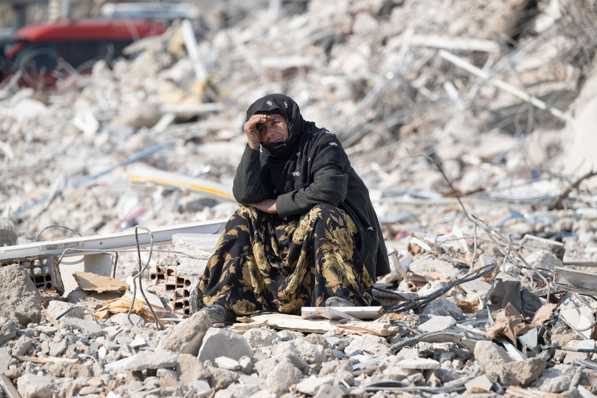 Eine Frau sitzt zwischen den Trümmern und beobachtet die Bergung von Opfern (Archivbild): Das Beben vor einem Monat in der Türkei und Syrien hat Zehntausende obdachlos gemacht und vertrieben.