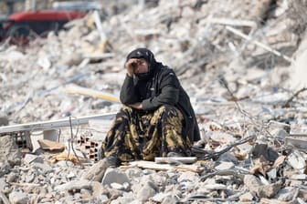 Eine Frau sitzt zwischen den Trümmern und beobachtet die Bergung von Opfern (Archivbild): Das Beben vor einem Monat in der Türkei und Syrien hat Zehntausende obdachlos gemacht und vertrieben.