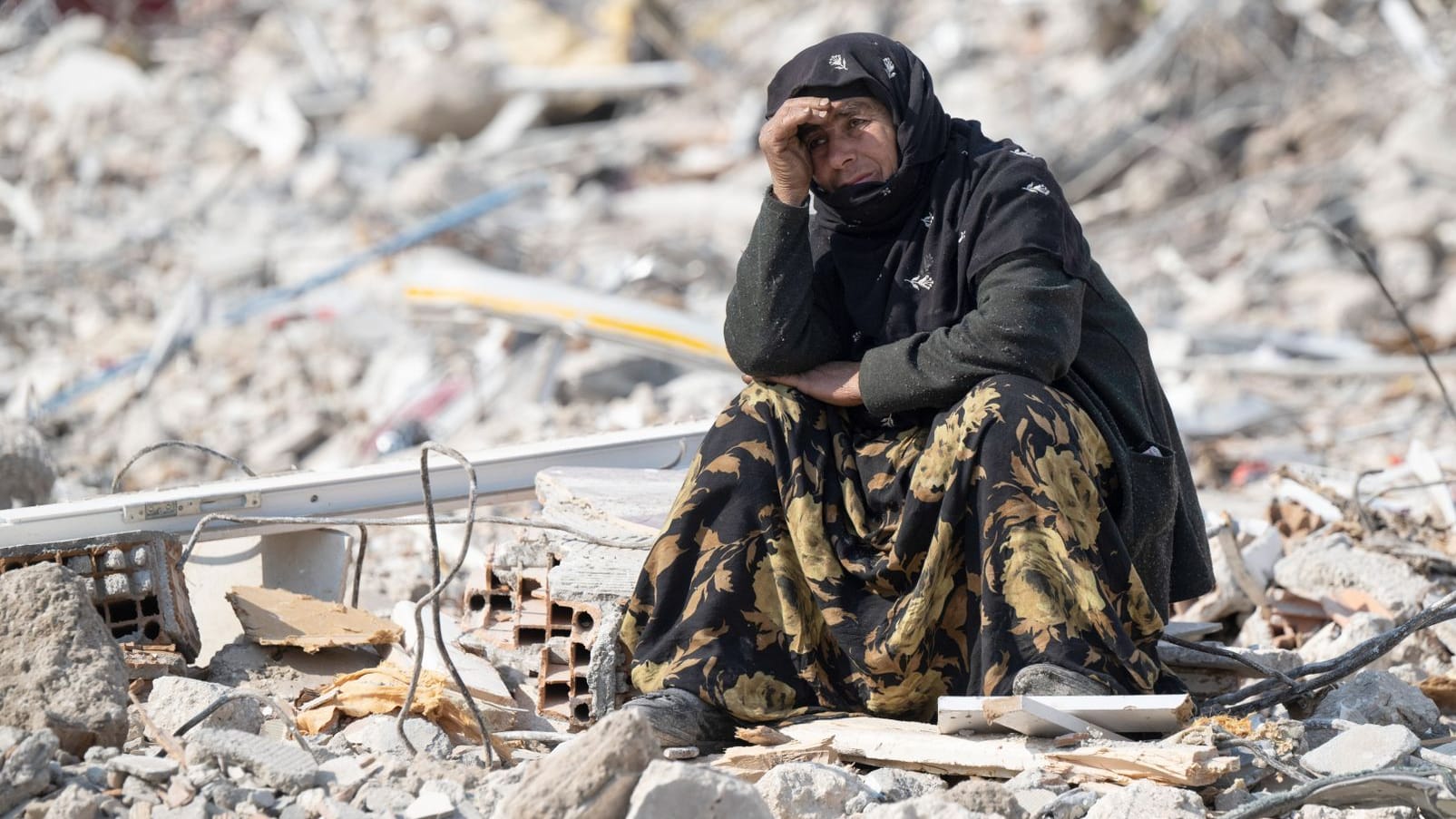 Eine Frau sitzt zwischen den Trümmern und beobachtet die Bergung von Opfern (Archivbild): Das Beben vor einem Monat in der Türkei und Syrien hat Zehntausende obdachlos gemacht und vertrieben.