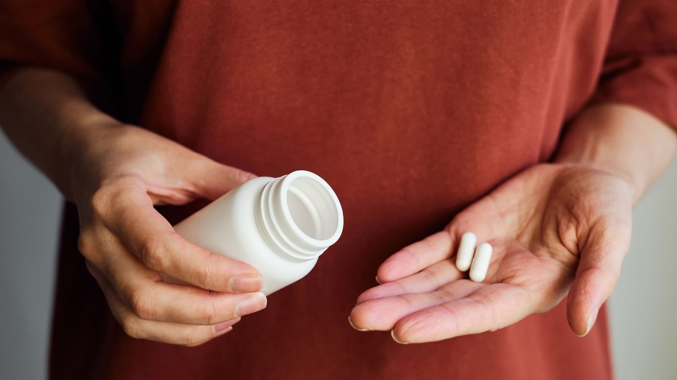 A woman holds a nutritional supplement and a glass of water in her hands.