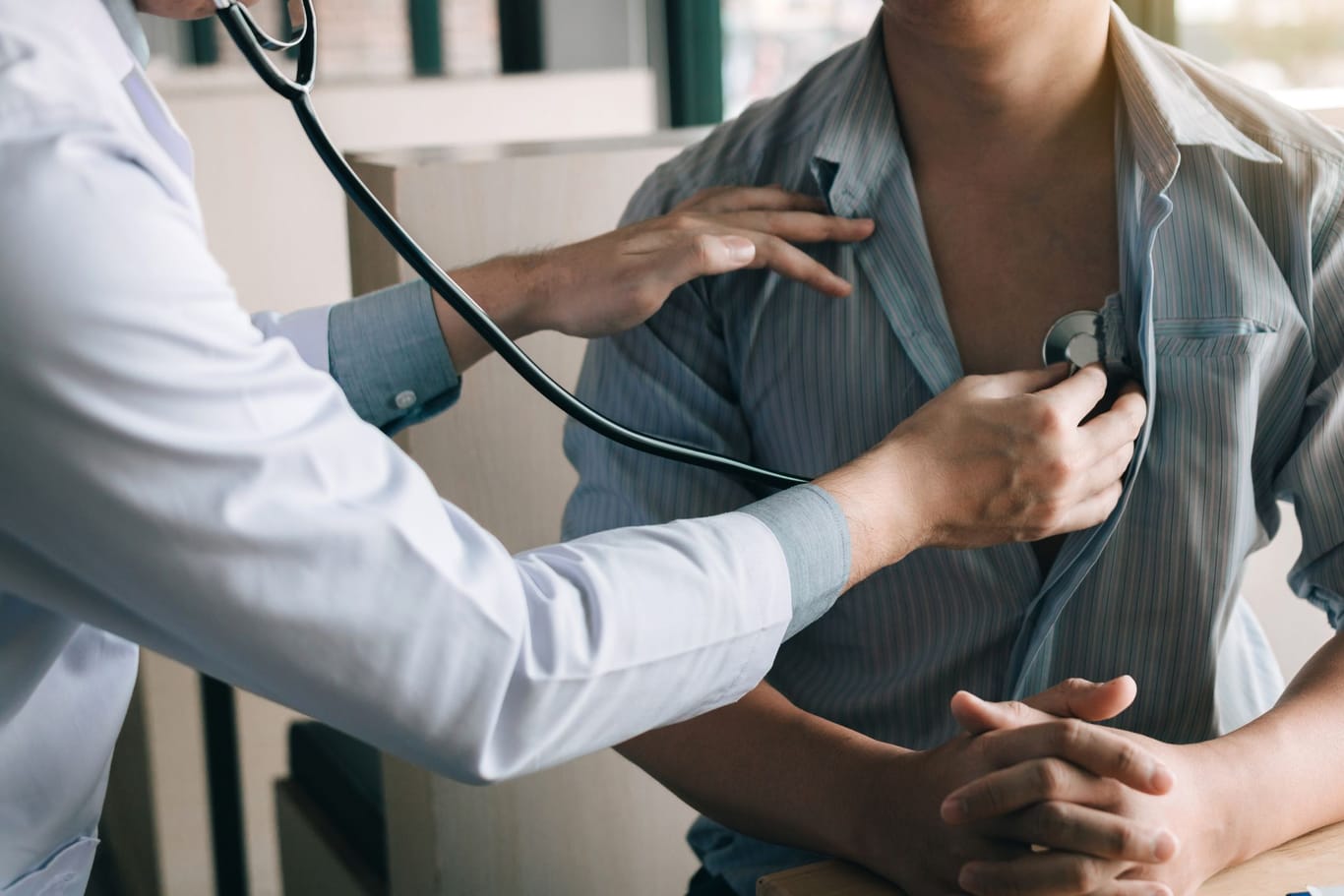 Ein Arzt hört mit einem Stethoskop das Herz eines Patienten ab.
