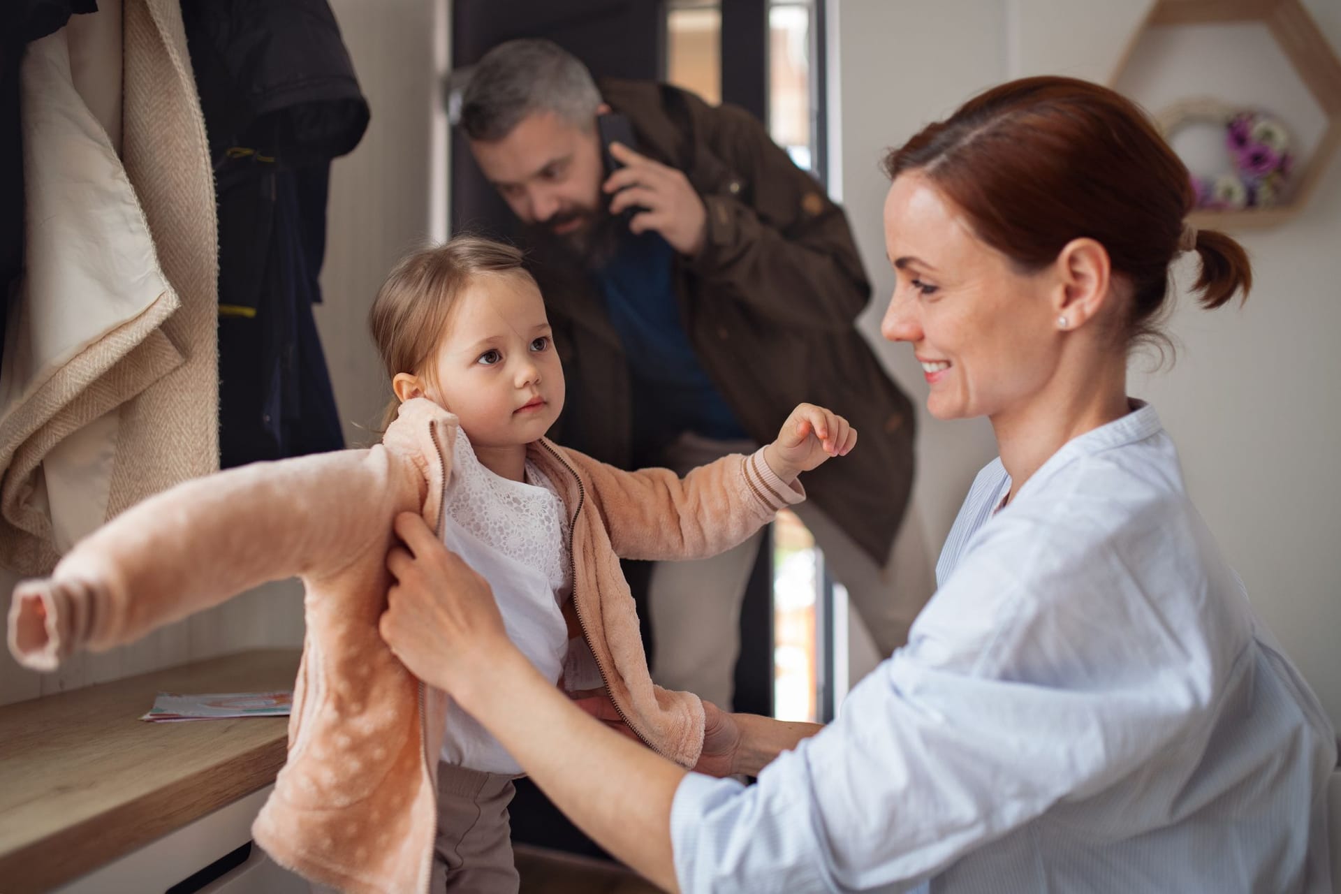 Vater telefoniert auf dem Weg zur Arbeit, Mutter macht die Tochter fertig für die Kita (Symbolbild): Familie und Beruf zu vereinen, ist noch immer eine Herausforderung.