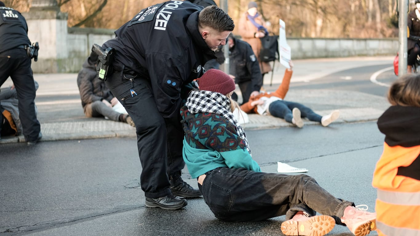 Ein Polizist zieht eine Aktivistin der "Letzten Generation" von einer Straße (Symbolfoto): Gegen eine 60-jährige Autofahrerin wurde Anzeige erstattet.