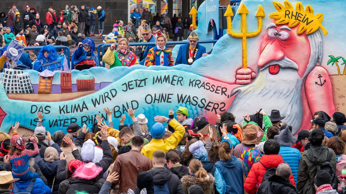 Rosenmontagszug in Düsseldorf 2023 mit einem Mottowagen zur Klimakrise. Der Schriftzug lautet: "Das Klima wird jetzt immer krasser, ist Vater Rhein bald ohne Wasser?"