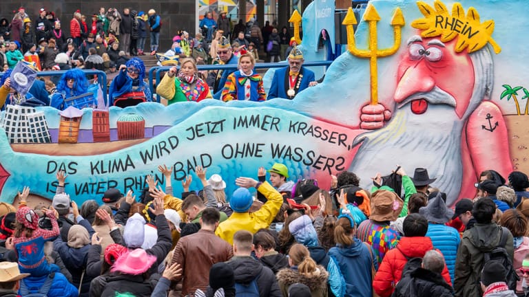 Rosenmontagszug in Düsseldorf 2023 mit einem Mottowagen zur Klimakrise. Der Schriftzug lautet: "Das Klima wird jetzt immer krasser, ist Vater Rhein bald ohne Wasser?"