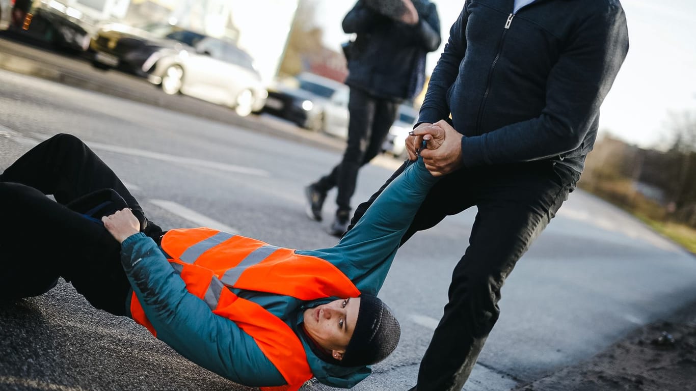Ein Aktivist wird von der Straße gezogen: Die erneute Blockadeaktion der "Letzten Generation" sorgt für Ärger bei den Verkehrsteilnehmern.