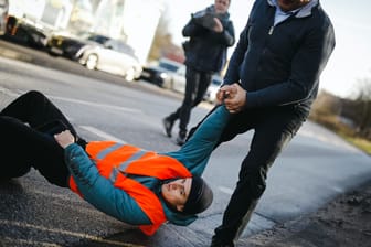 Ein Aktivist wird von der Straße gezogen: Die erneute Blockadeaktion der "Letzten Generation" sorgt für Ärger bei den Verkehrsteilnehmern.