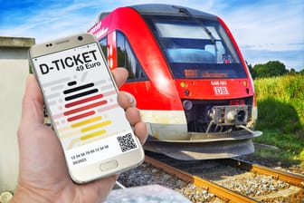 Hand hält ein Smartphone mit D-Ticket, Deutschlandticket vor einer Regionalbah