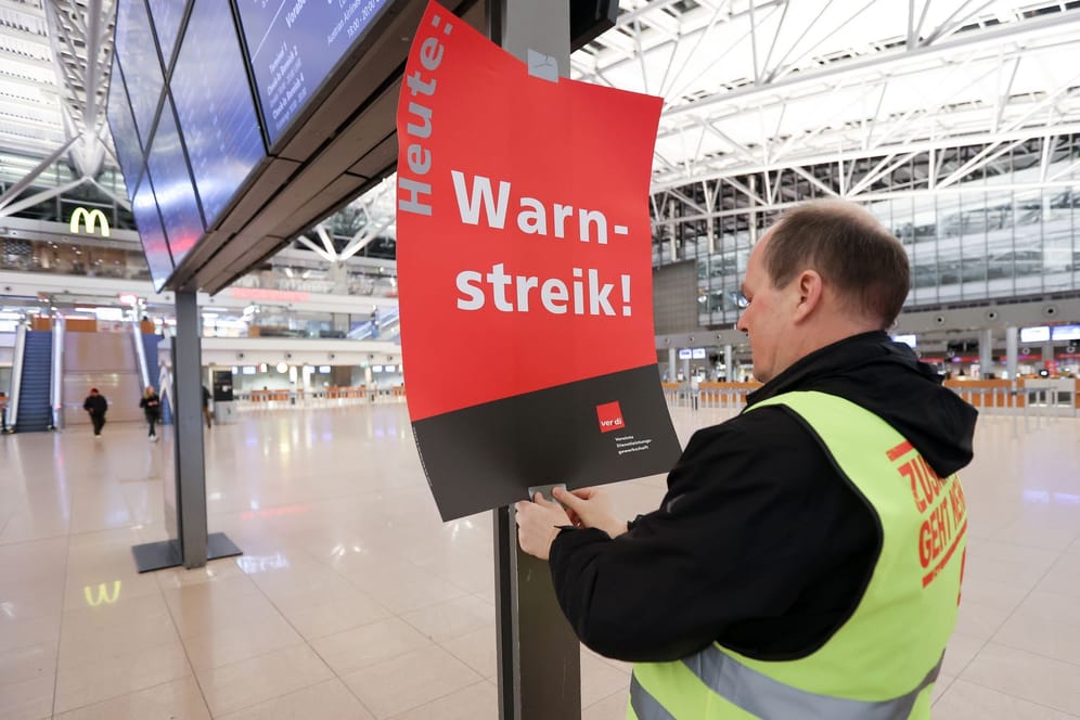 Ein Gewerkschaftsvertreter klebt ein Plakat mit der Aufschrift "Warnstreik!" an die Anzeigetafel vor das leere Terminal 1 in Hamburg.