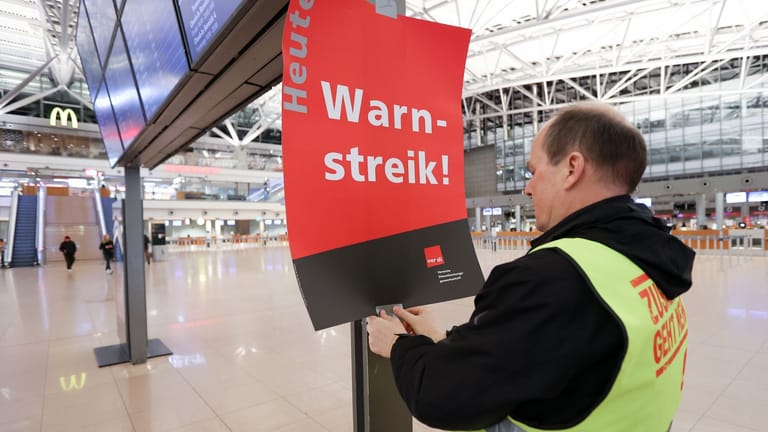 Ein Gewerkschaftsvertreter klebt ein Plakat mit der Aufschrift "Warnstreik!" an die Anzeigetafel vor das leere Terminal 1 in Hamburg.
