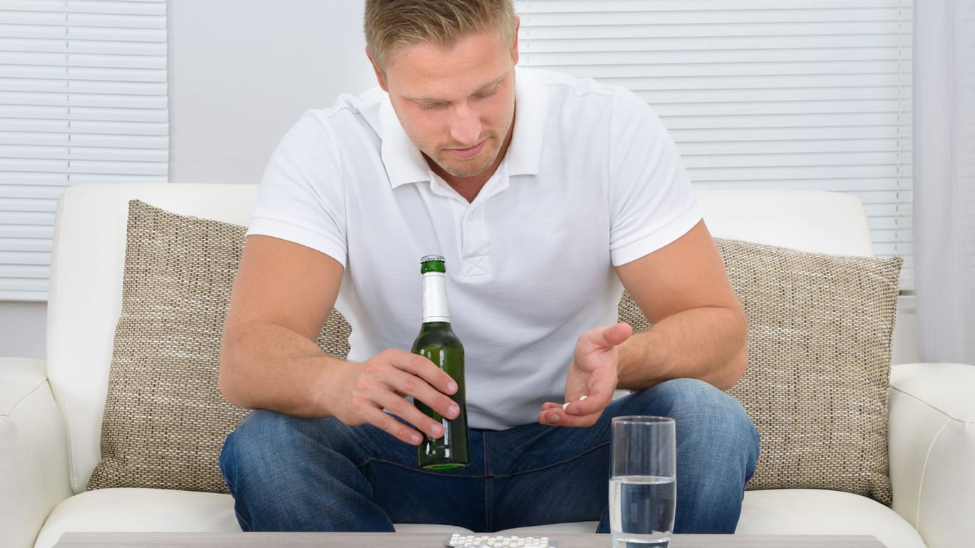 Mann mit Tabletten in der linken und einer Bierflasche in der rechten Hand.