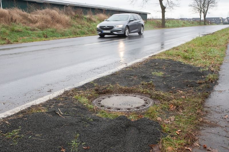 Der Kanaldeckel neben einer Landstraße in Niederkassel-Lülsdorf: Hier hat ein Passant eine kopfüber steckende Leiche in einem Kanalschacht entdeckt hat.