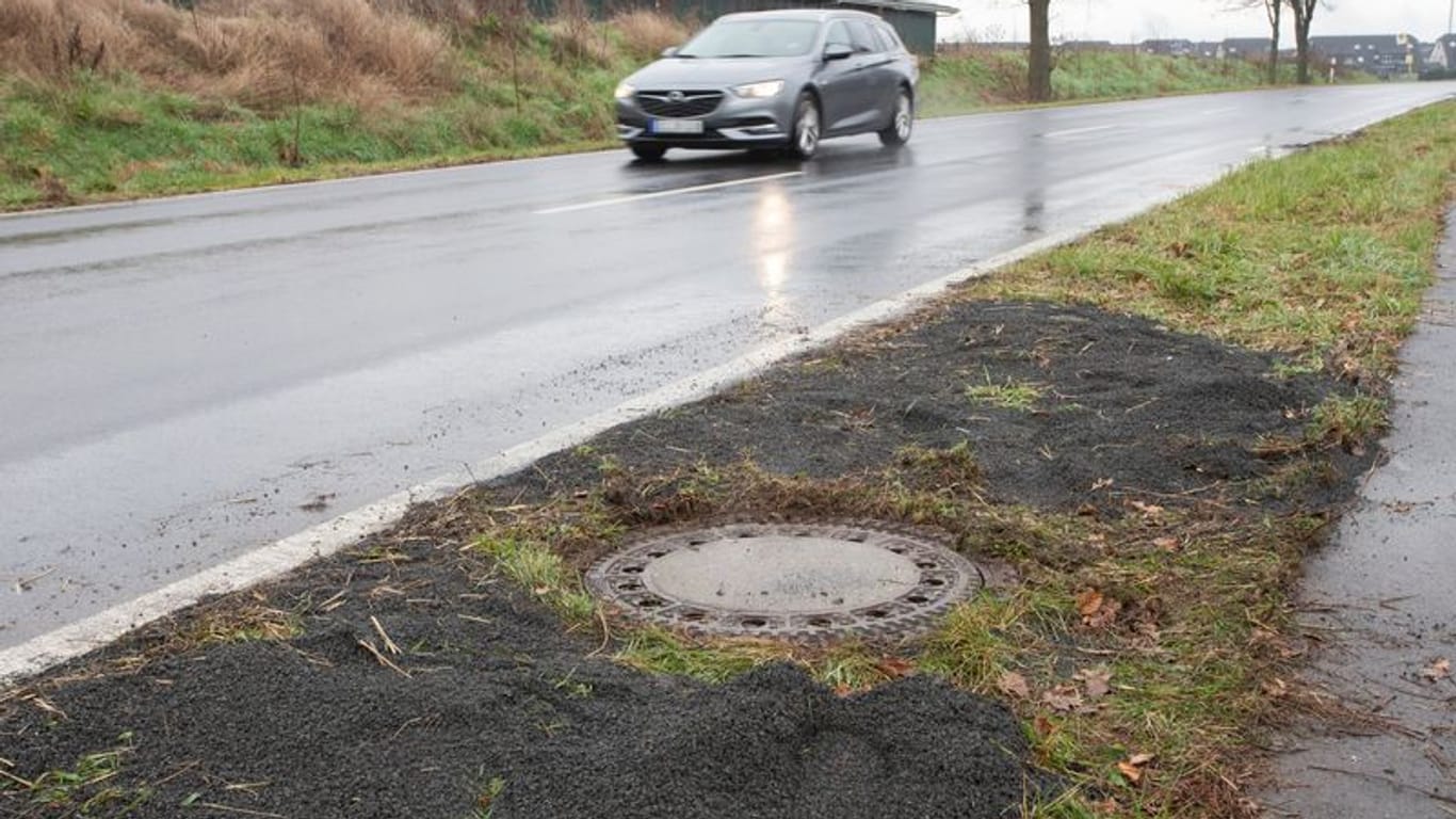 Der Kanaldeckel neben einer Landstraße in Niederkassel-Lülsdorf: Hier hat ein Passant eine kopfüber steckende Leiche in einem Kanalschacht entdeckt hat.