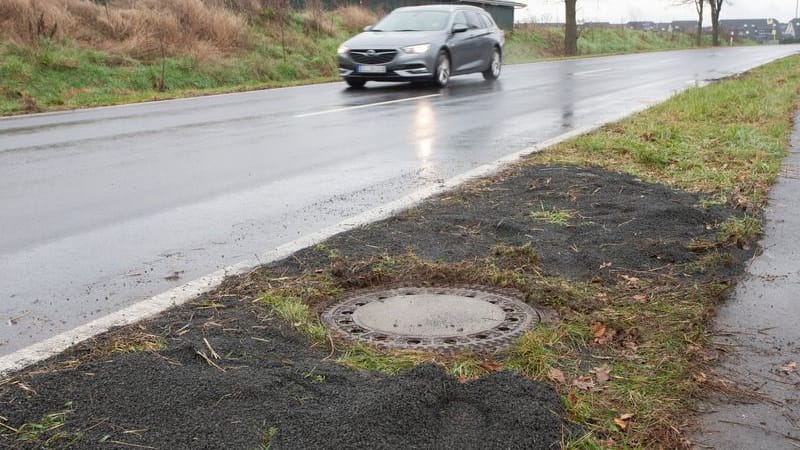 Der Kanaldeckel neben einer Landstraße in Niederkassel-Lülsdorf: Hier hat ein Passant eine kopfüber steckende Leiche in einem Kanalschacht entdeckt hat.