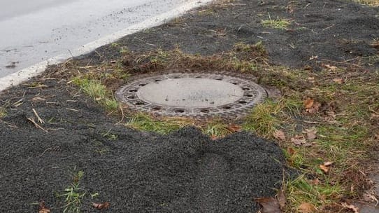 Der Kanaldeckel neben einer Landstraße in Niederkassel-Lülsdorf: Hier hat ein Passant eine kopfüber steckende Leiche in einem Kanalschacht entdeckt hat.