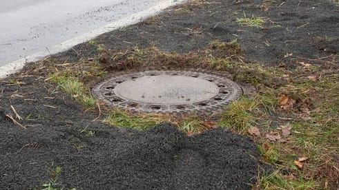 Der Kanaldeckel neben einer Landstraße in Niederkassel-Lülsdorf: Hier hat ein Passant eine kopfüber steckende Leiche in einem Kanalschacht entdeckt hat. Der Kanaldeckel neben einer Landstraße in Niederkassel-Lülsdorf: Hier hat ein Passant eine kopfüber steckende Leiche in einem Kanalschacht entdeckt hat.