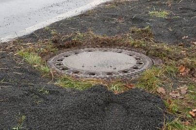 Der Kanaldeckel neben einer Landstraße in Niederkassel-Lülsdorf: Hier hat ein Passant eine kopfüber steckende Leiche in einem Kanalschacht entdeckt hat.