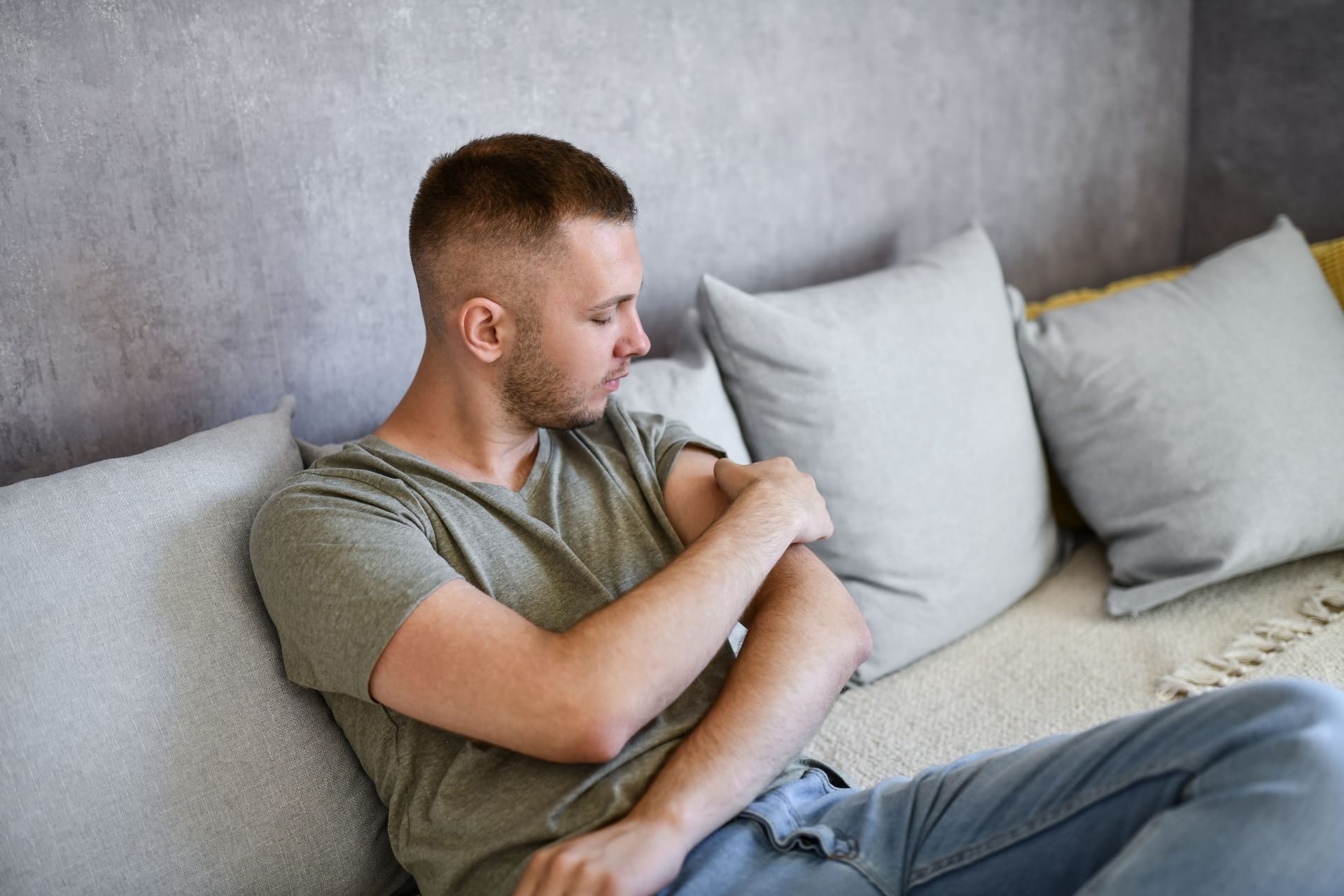 Ein Mann sitzt auf dem Sofa und betrachtet seinen linken Oberarm.