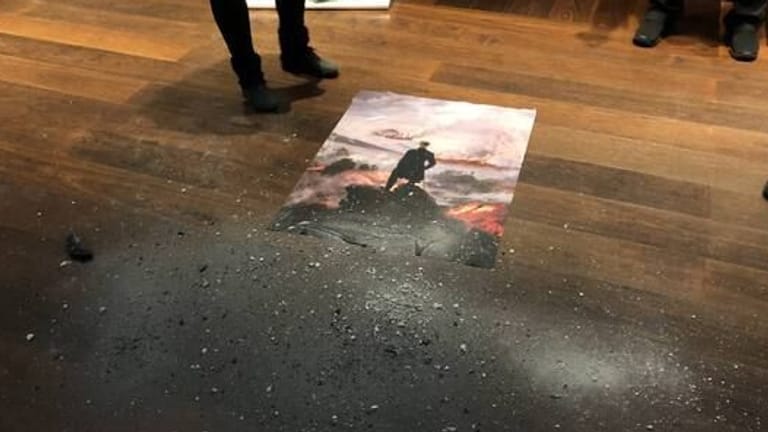 Ein Poster wurde auf dem Boden liegend mit Asche bestreut: Statt Wäldern im Nebel ist ein Waldbrand im Hintergrund zu sehen.