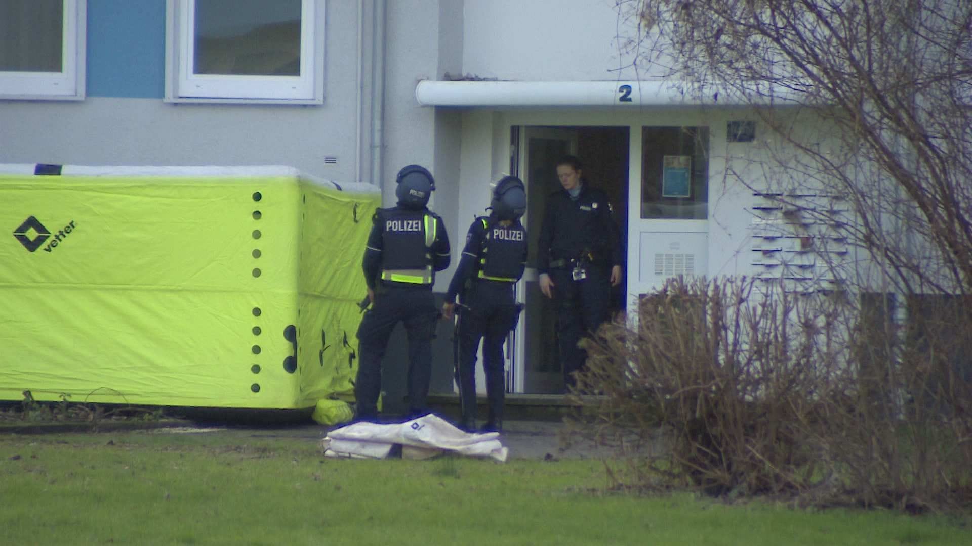 Der Eingang des Wohnhausblocks: Polizisten mit Helmen und Schutzwesten stehen im Eingang des Hauses.