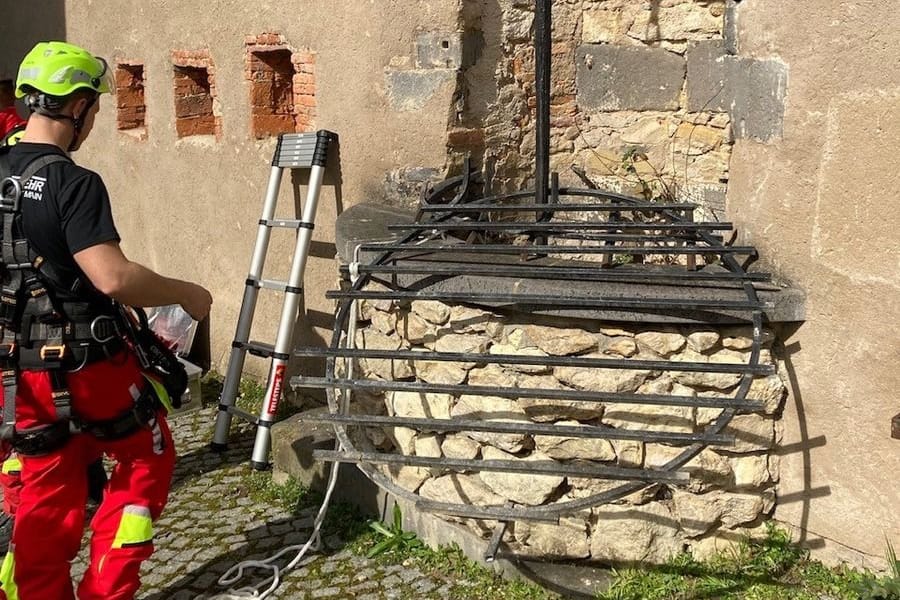 Ein Feuerwehrmann steht vor dem Brunnen: Er seilte sich zur Katze herab und konnte sie aus dem Brunnen holen.