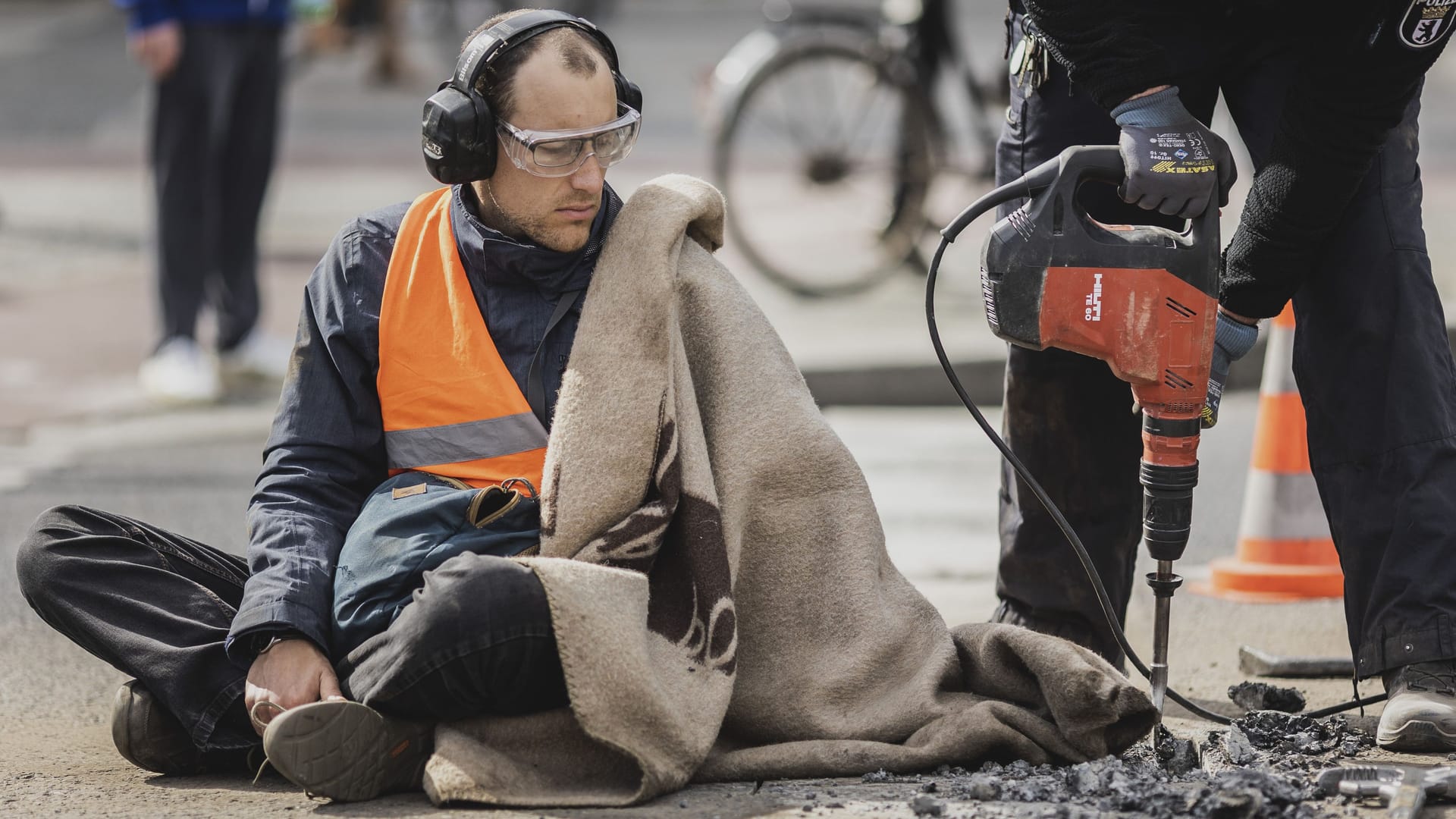 Ein Aktivist der Protestbewegung 'Letzte Generation', wird mit einer Schlagbohrmaschine in Berlin von der Straße entfernt.