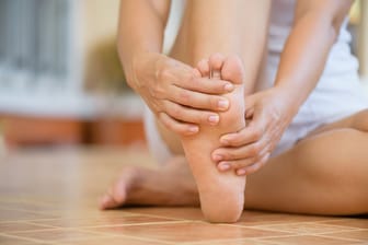 Auf dem Boden sitzende Frau umschließt ihren rechten Fuß mit den Händen: Eine Plantarfasziitis lässt sich mit verschiedenen Maßnahmen behandeln.