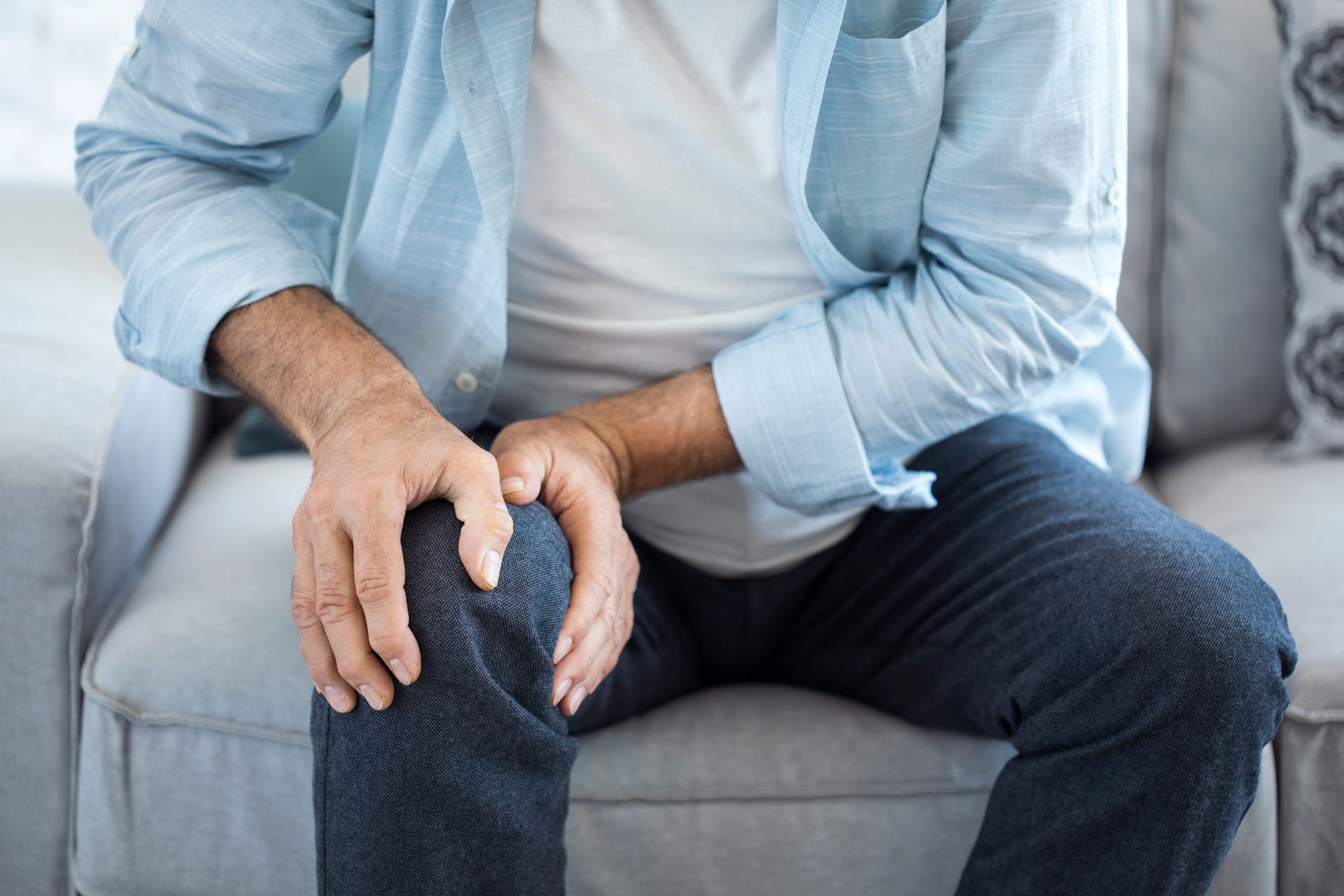 Ein Mann sitzt auf dem Sofa und fasst sich ans Knie.