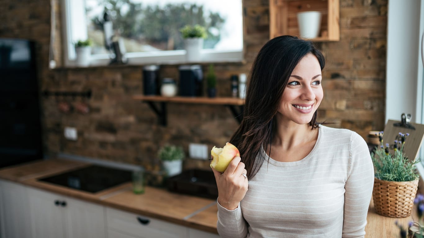 Eine Frau isst einen Apfel und lächelt.