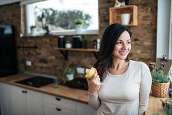 Eine Frau isst einen Apfel und lächelt.